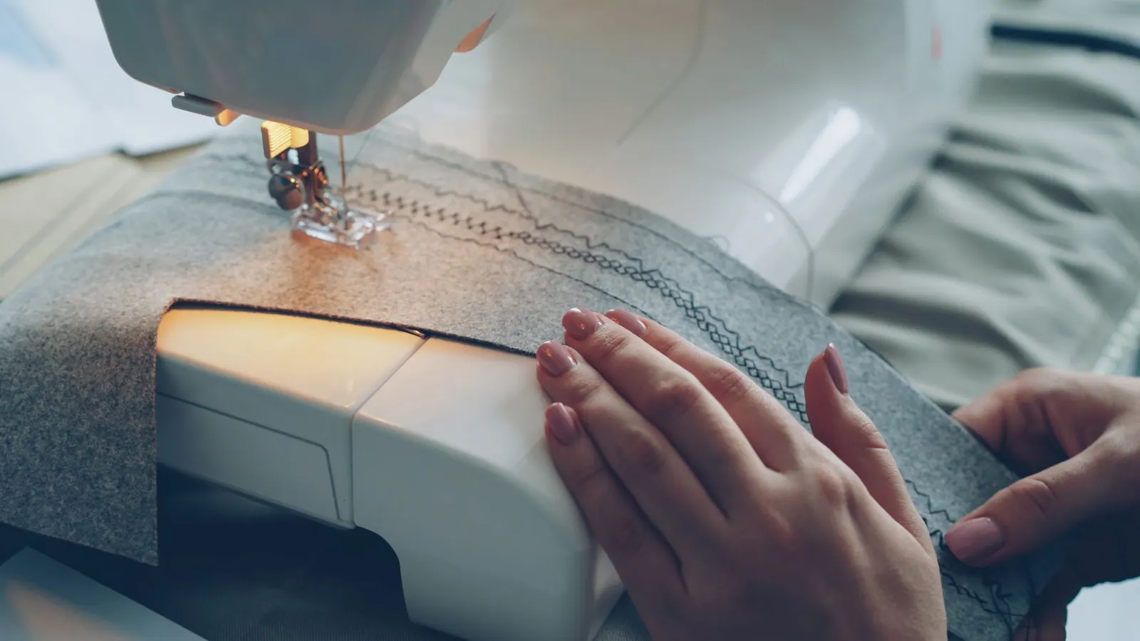 Hands guiding fabric through a sewing machine, stitching pattern.