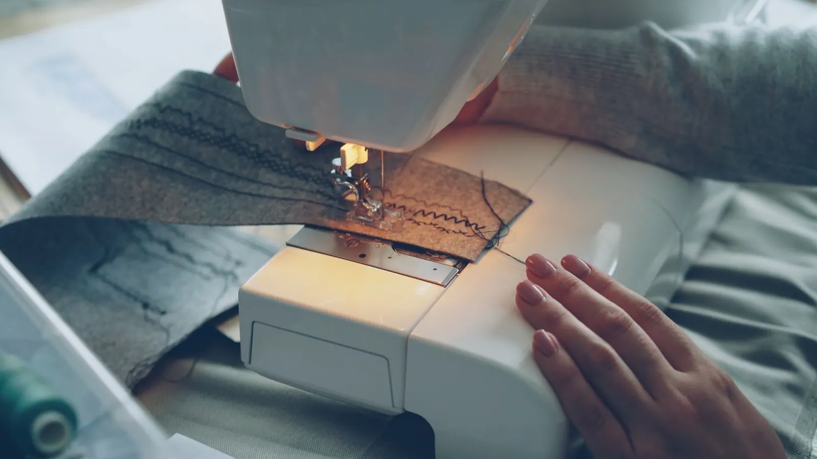 Close-up of a sewing machine stitching fabric, focused on hands and textile.