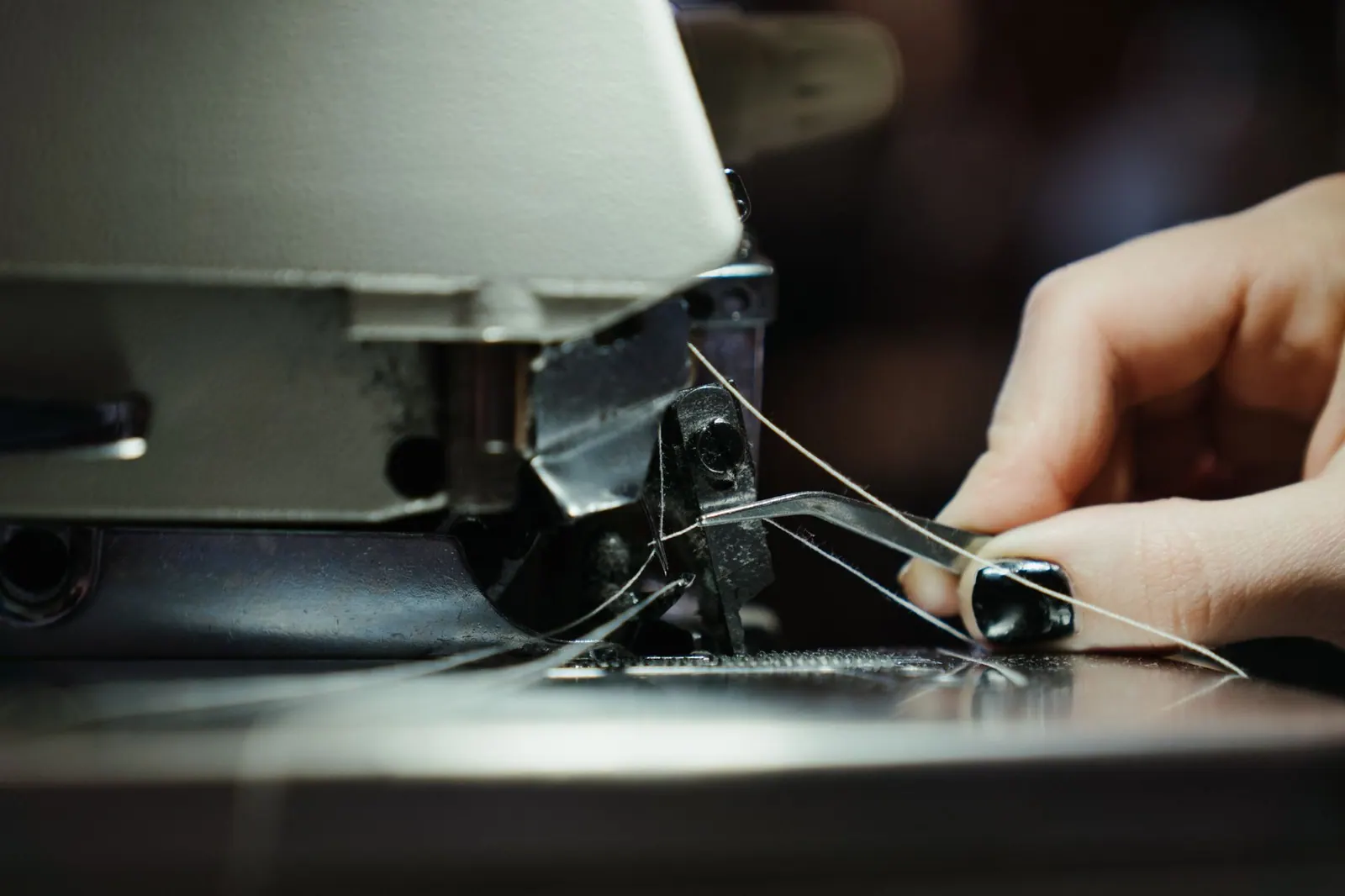 Detailed close-up of a sewing machine in use, highlighting the threading process with a human hand. Booking, triage and deposits: a solo sewing repair business week explained