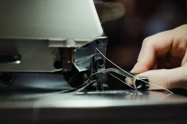 Detailed close-up of a sewing machine in use, highlighting the threading process with a human hand. Booking, triage and deposits: a solo sewing repair business week explained