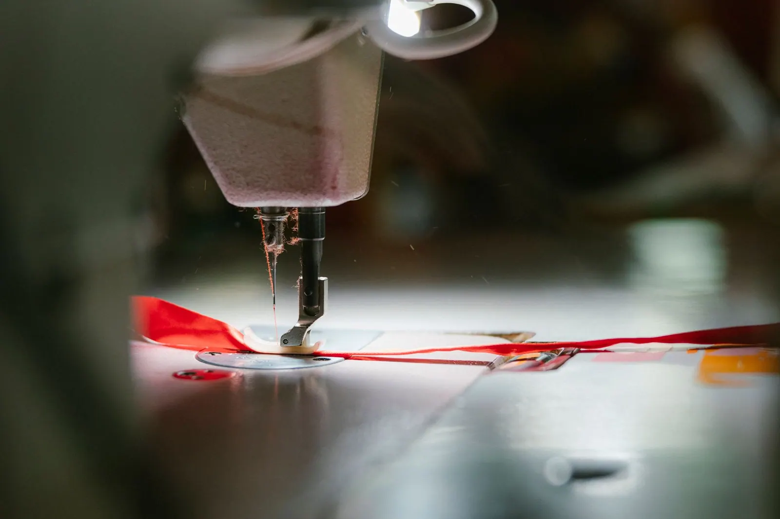 A focused view of a sewing machine needle stitching fabric under bright lights, showcasing precision.
