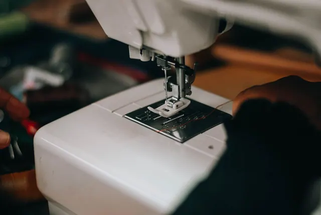 Detailed close-up of hands using a sewing machine, focusing on the needle and fabric.