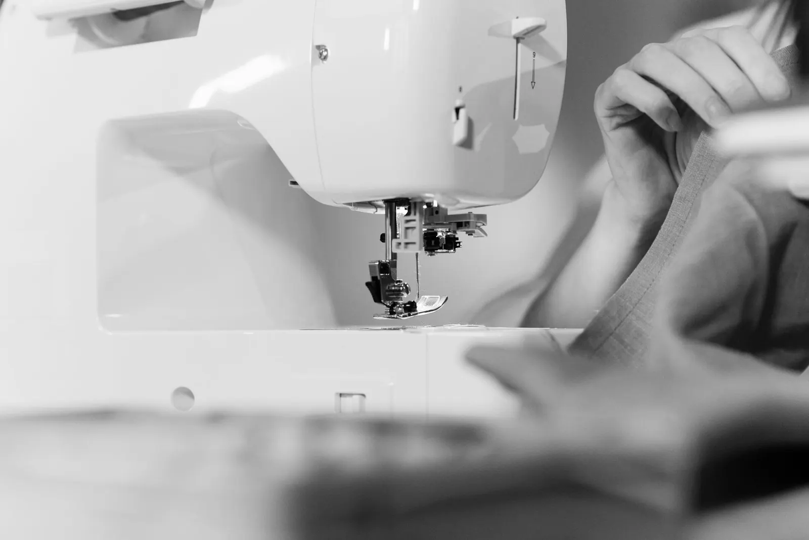 Detailed view of a sewing machine in action, stitching fabric in black and white.