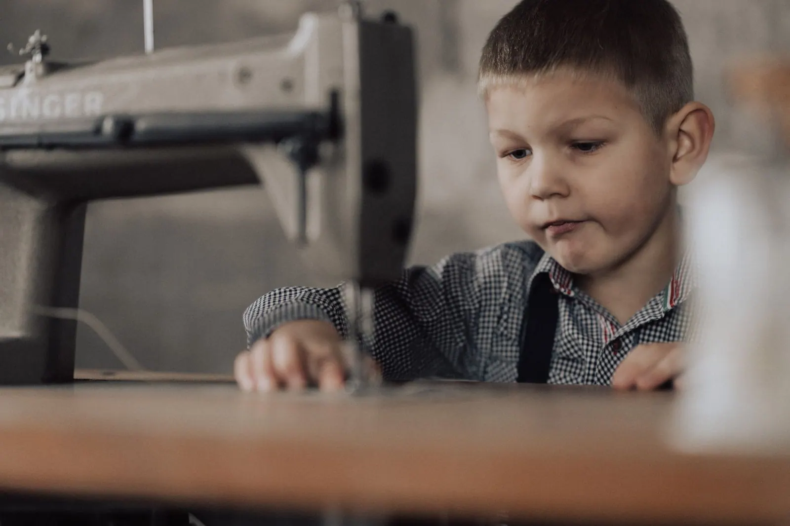 A young boy focuses intently while sewing with a vintage machine indoors.