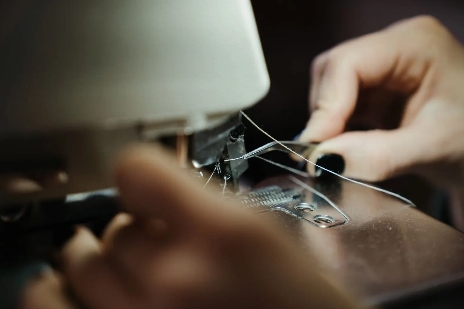 A close-up of hands threading a sewing machine in a workshop setting.